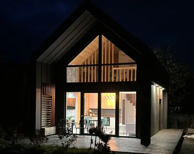 Nowoczesny dom szkieletowy z drewnianą elewacją i ciemnym dachem, wyposażony w taras na dachu z miejscem do wypoczynku.