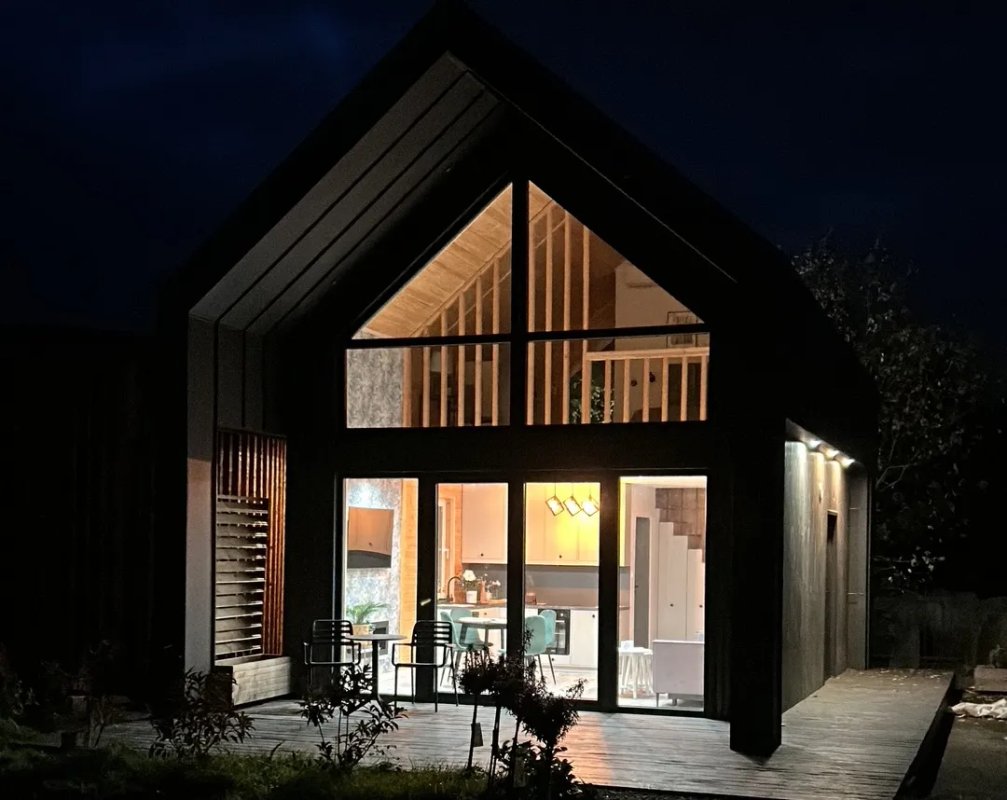 Nowoczesny dom szkieletowy z drewnianą elewacją i ciemnym dachem, wyposażony w taras na dachu z miejscem do wypoczynku.