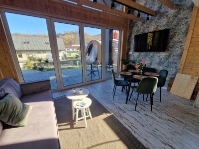 Salon z aneksem w Ekodom50: szara sofa, okrągłe stoliki, stół, TV, dekoracje.