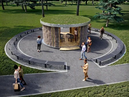 Widok z góry na okrągłą tężnię solankową Small Salty Rest z zielonym dachem porośniętym trawą, otoczoną alejką spacerową z ławkami. Wokół tężni i w jej wnętrzu spacerują ludzie. Tężnia ma elewację z naturalnych materiałów, a w tle widać drzewa i zielony trawnik.