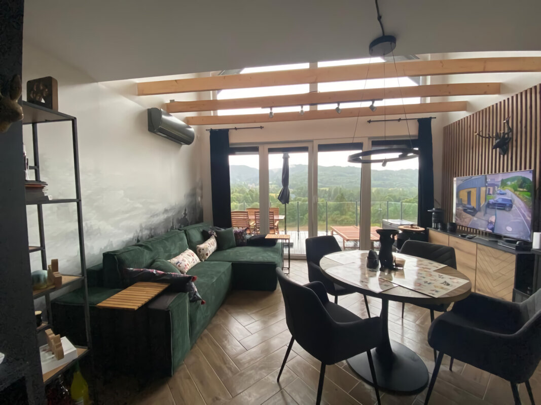 Helles Wohn-/Esszimmer mit grünem Sofa und Aussicht; Skelettbauweise, große Verglasung.