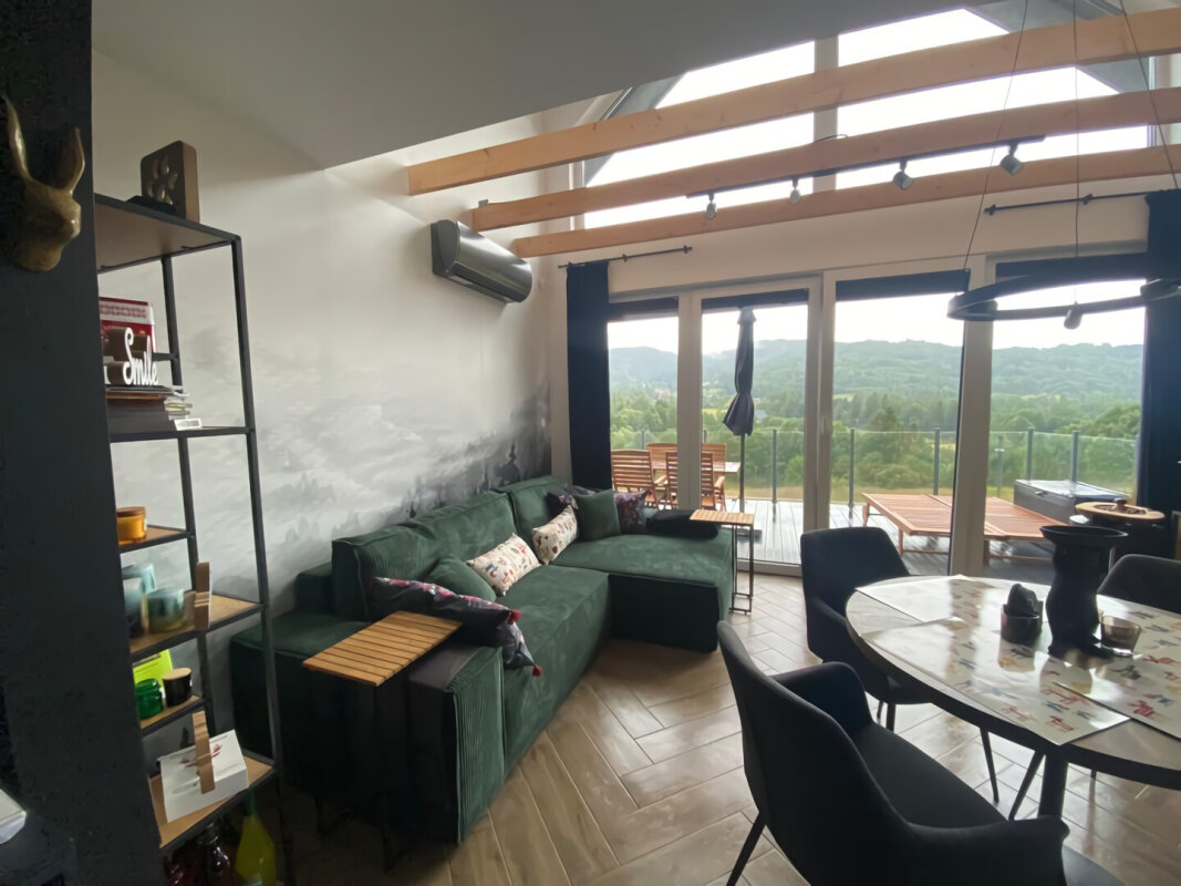 Innenraum eines Freizeit-Skeletthauses; grünes Sofa, Holzboden, Verglasung, Klimaanlage.