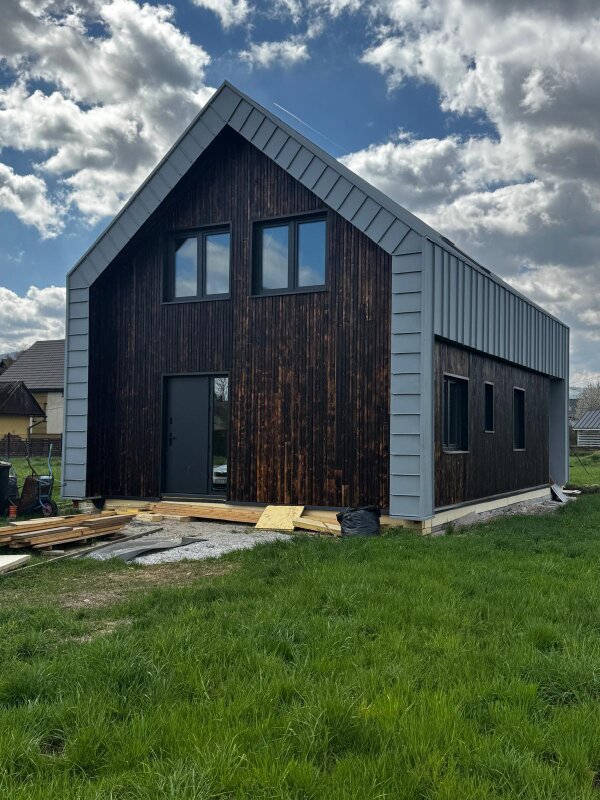 Widok na dwukondygnacyjny budynek szkieletowy w trakcie montażu elewacji oraz stolarki okiennej