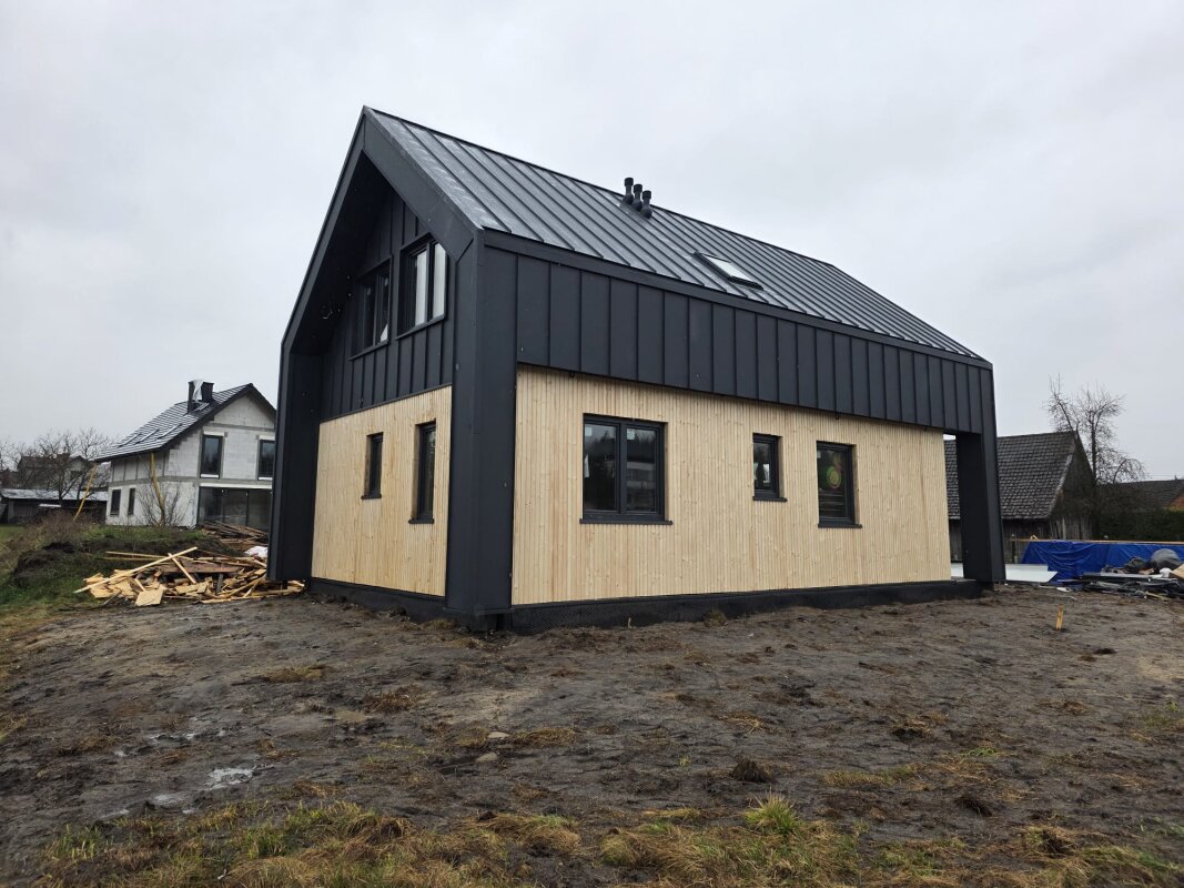 Bryła domu szkieletowego w Dziewinie z widocznym dachem krytym blachą na rąbek oraz elewacją łączącą deskę z ciemnymi panelami