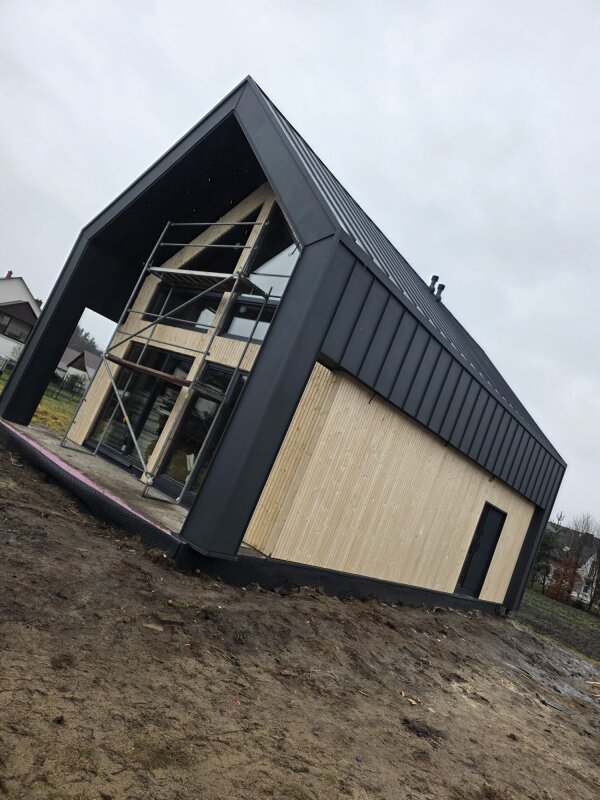 Widok od frontu na dom szkieletowy w Dziewinie z widocznymi przeszkleniami antresoli i rusztowaniem w trakcie montażu