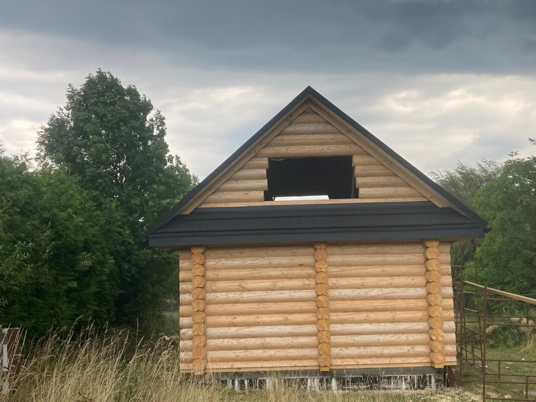 Spruce log house in Brenna; gable end facade, black roof, shell state.