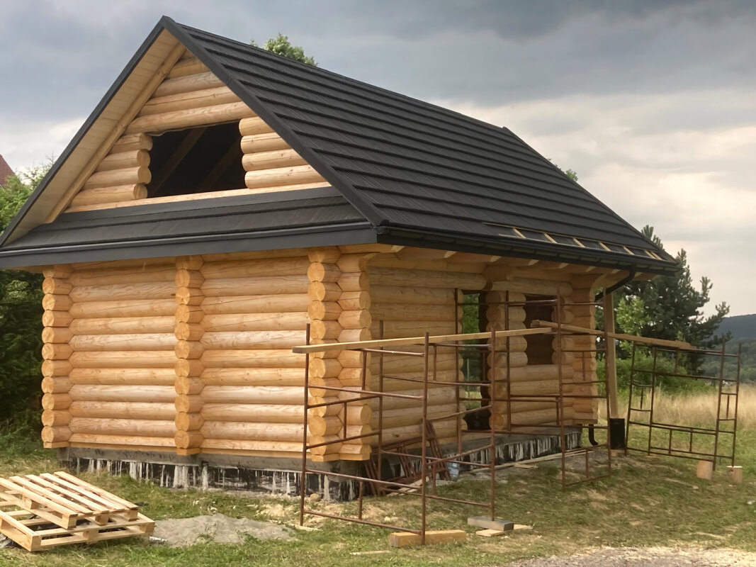 All-year log house from spruce in Brenna, black roof, construction stage.