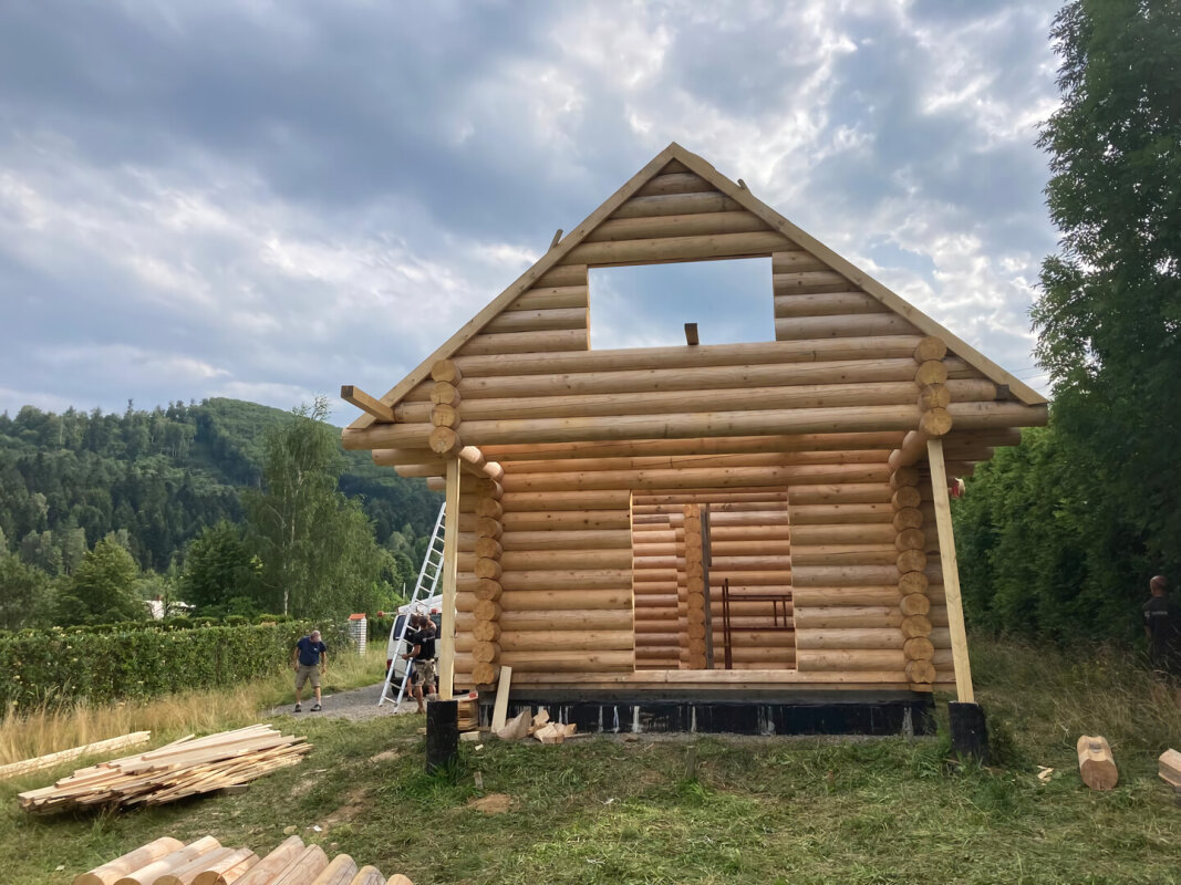 Front of the log house in Brenna; upstairs window opening, mountain landscape.