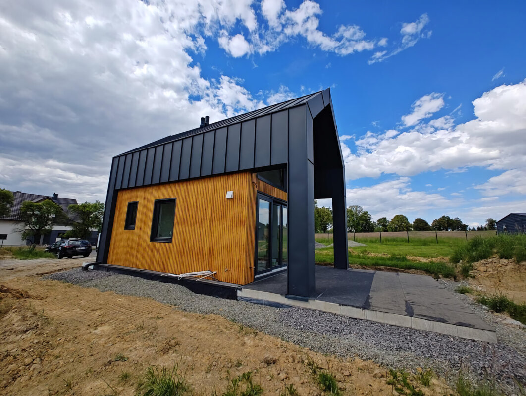 Elewacja tylna domu szkieletowego, przeszklenia tarasowe, zadaszenie w czarnej ramie.