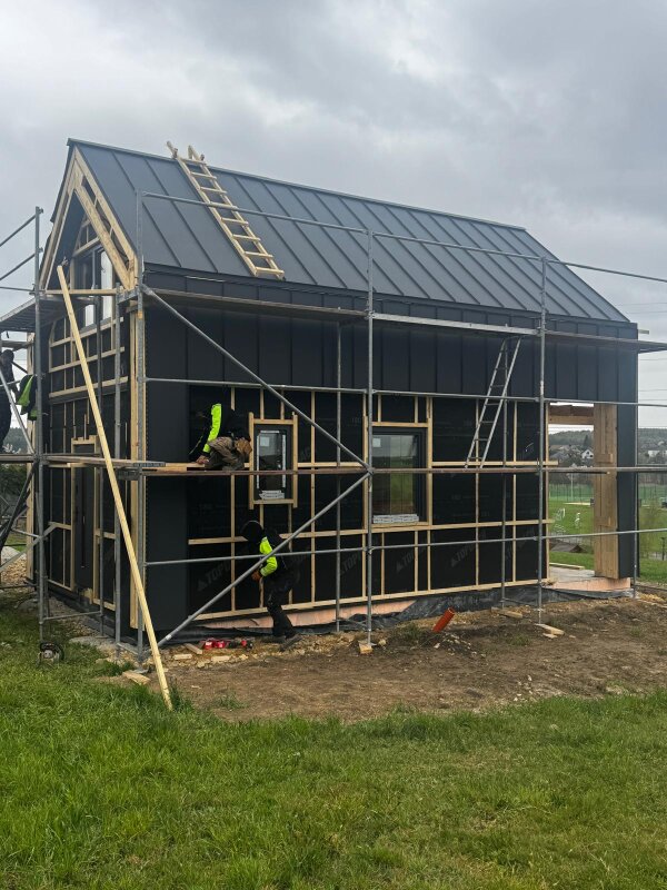 Frontowa część budynku szkieletowego w trakcie budowy z widocznym otworami okiennymi i konstrukcją dachu