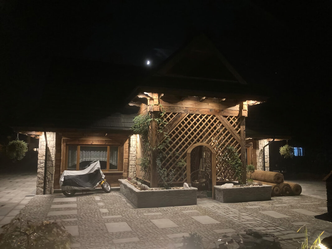 Highlander log house at night, illuminated truss porch and wooden facade