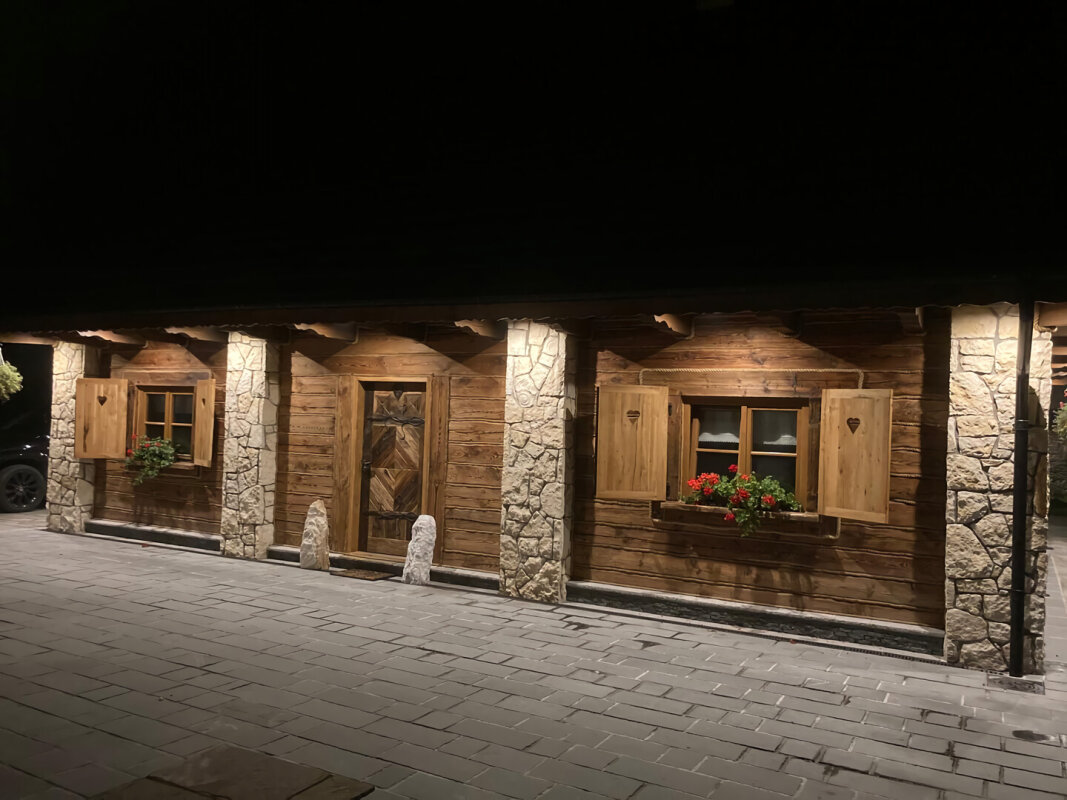 Log house facade at night, stone pillars and heart-shaped shutters