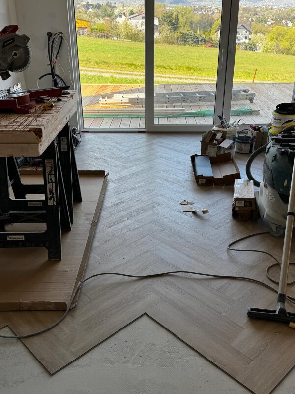 Wnętrze domu szkieletowego w trakcie prac wykończeniowych z widoczną podłogą układaną w jodełkę