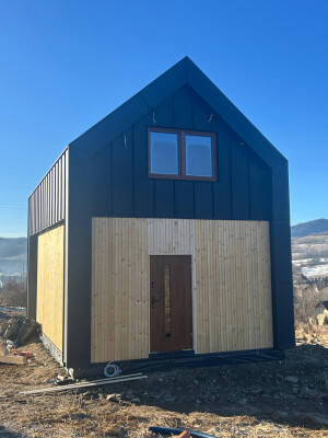 Vorderseite des Hauses Ekodom 50, Eingangstür, Holz- und schwarze Blechverkleidung.