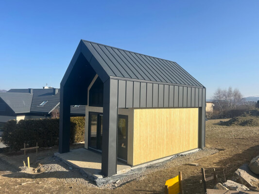 Seitenansicht des Holzrahmenhauses Ekodom 50: schwarzes Stehfalzblech und helle Holzfassade.